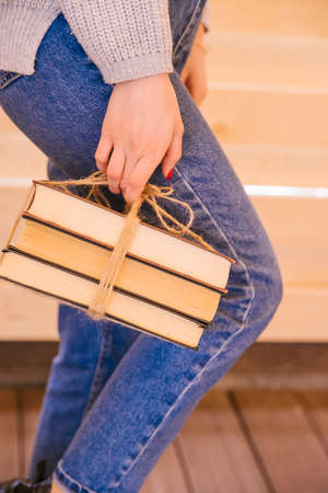 A young woman holds books tied with twine in her hands. The girl is wearing a sweater and jeans. Student and schoolboy. Books from the library.の写真素材