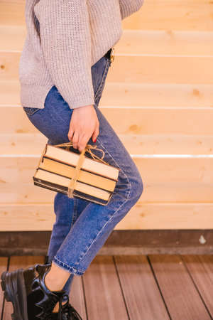 A young woman holds books tied with twine in her hands. The girl is wearing a sweater and jeans. Student and schoolboy. Books from the library.の写真素材