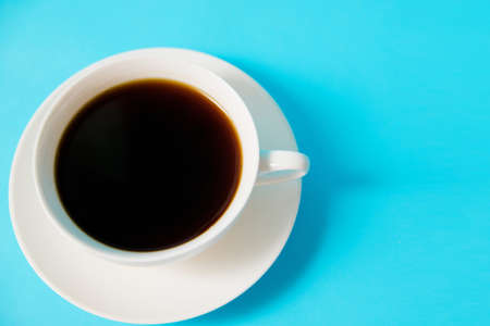 White cup with black coffee on a blue background. Morning breakfast.Empty space for the text. Minimalistic photography.の写真素材
