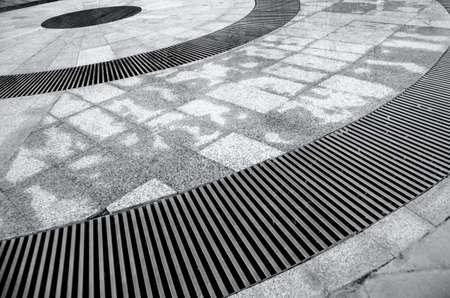 The grate of the city fountain drain. Texture and background of metal grating and stone. Rough...