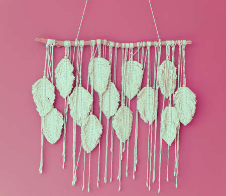 Macrame hangs on the pink wall. The fringe is white in close-up. The interior is finished by hand. Texture of threads and textiles.Decoration of the interior of the room.の写真素材