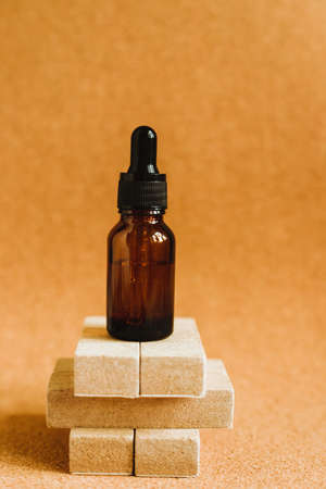 Cosmetic oil in a container with an eyedropper is on the podium. Essential oil for aromatherapy. The bottle is brown. Beige is the natural color of the composition.の写真素材
