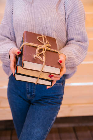 A young woman stands and holds a stack of books in her hands. Books tied with string. The girl is a student, preparing for college or an exam.の写真素材