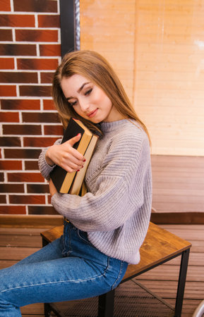 A beautiful girl in a gray knitted sweater reads a book in a cozy cafe, the concept of pleasant...
