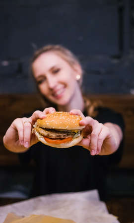 A young girl holds a burger with a meat patty in her hands. Delicious and hearty lunch. Fast food and snacks. The girl smiles.の写真素材