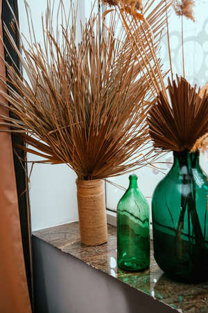 Dried palm leaves and reed branches in glass jars. Home decor stands on the windowsill. Trendy style in the interior.の写真素材