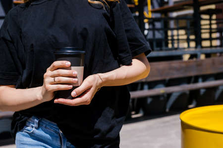 A young woman stands outside on a bright sunny day. The girl is holding a paper cup of coffee. Walking around the city, a way of life.の写真素材
