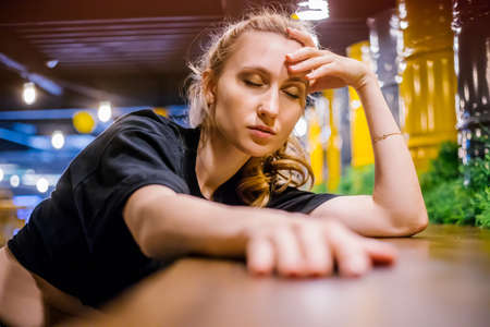 A young woman sits at a table in a cafe with a thoughtful look. She put her head in her hands. The concept of unresolved problems, fatigue and stress.の写真素材