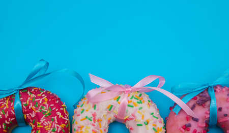 Sweet donuts of different colors are arranged in a row on a blue background. Confectionery products. Harmful fast food.Bright colored background. Donuts decorated with ribbon bows.の写真素材