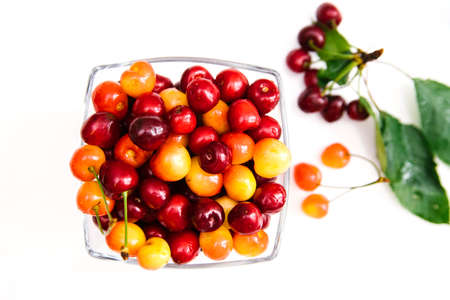 Ripe red and yellow cherries in a glass cup. Juicy cherry with leaves on a white background. Light snack. Fruit salad for breakfast. Diet.の写真素材