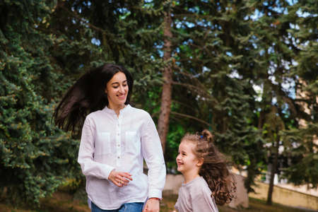 A little girl and her mother run along the sidewalk in the park. Active play in nature. The girl laughs and is happy. Spring time of the year. Warm sunny weather.Close-up photo.の写真素材
