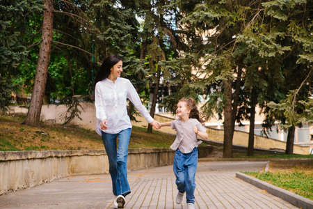 A little girl with her mother runs along the sidewalk in the park. Active play in nature. The girl laughs and is happy. Spring time of the year. Warm sunny weather.の写真素材