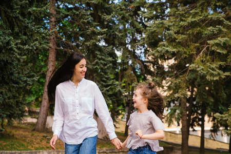 A little girl and her mother run along the sidewalk in the park. Active play in nature. The girl laughs and is happy. Spring time of the year. Warm sunny weather.Close-up photo.の写真素材
