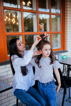 A beautiful young woman fixes her little daughter's hair. Family leisure and recreation. Motherly care and love. Mother's Day and March 8.の写真素材