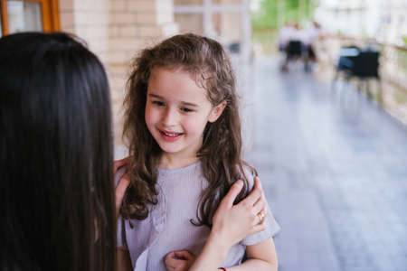 A young woman is talking to her little daughter. The girl listens attentively to her mother. The family is relaxing in a cafe on the street.の写真素材