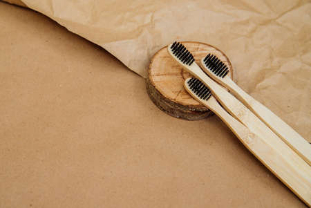Three toothbrushes made of natural bamboo are lying on a piece of wood, against a background of brown kraft paper. A sustainable lifestyle and a plastic-free concept, bathroom essentials.の写真素材