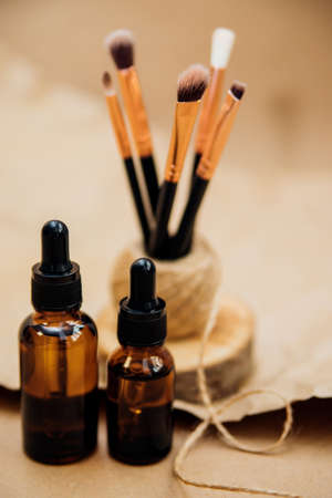 Cosmetic oil in a container with a pipette. Makeup brushes stand on a podium made of sawn wood. Essential oil for aromatherapy.Monochrome image.の写真素材