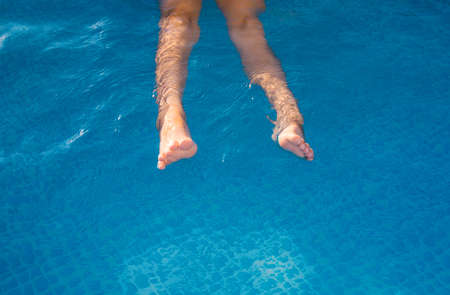 A child is swimming in the pool. In the frame, the legs are in clear water. Summer holidays and...