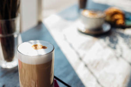 Latte in a tall glass on a blurry background. The drink is on the table in the cafe. Delicious breakfast and snack. Pleasant leisure and recreation.の写真素材