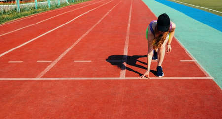 A sporty woman stands at the start of the treadmill at the stadium. Sportswear. A bright sunny day...