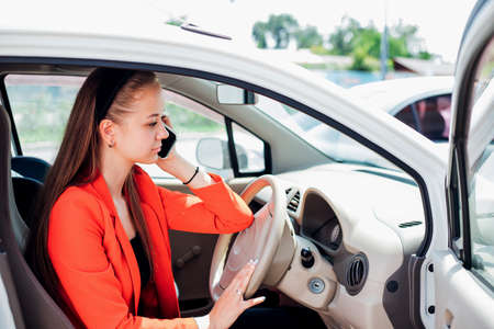 A young woman is sitting at the wheel of a car and talking on a mobile phone. Transport...