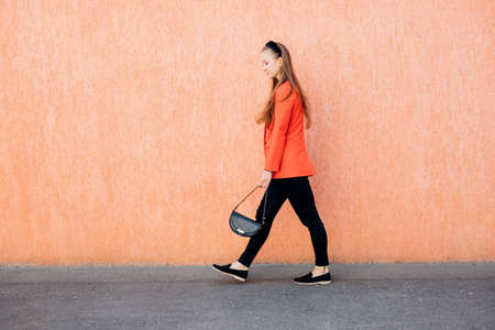 A happy young woman with a bag in her hands is walking down the street. A cheerful girl in a stylish suit, a confident business lady, ready for an office meeting.の写真素材