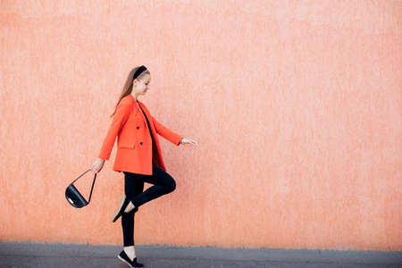 A happy young woman with a bag in her hands poses on a pink background. A cheerful girl in a stylish suit, a confident business lady, ready for an office meeting.の写真素材