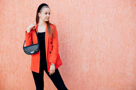 A happy young woman with a bag in her hands poses on a pink background. A cheerful girl in a stylish suit, a confident business lady, ready for an office meeting.の写真素材