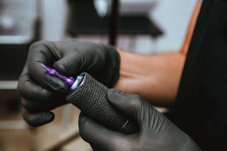 Young male hands in black gloves are setting up a tattoo machine. Preparation for work. Small business.の写真素材
