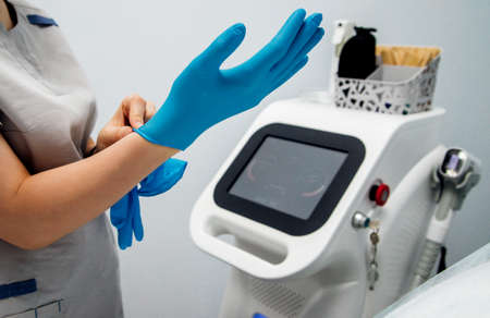 A young woman's hands are put on medical gloves, preparing for the laser hair removal procedure. Skin care, cosmetic procedures.の写真素材