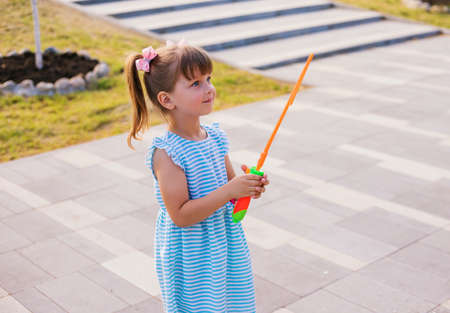 In a public park, a little girl blows and catches soap bubbles. The child is playing and laughing. The bubbles shimmer in the sun and fly in different directions.の写真素材