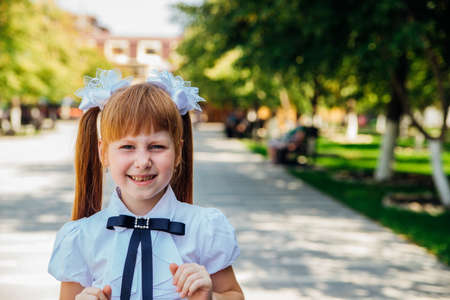 A little girl, an elementary school student, is standing on the street, a schoolgirl is laughing and...