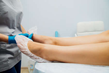 Women's hands in blue gloves put disposable socks on the client's feet. Beauty salon or medical procedures. Massage or pedicure.の写真素材