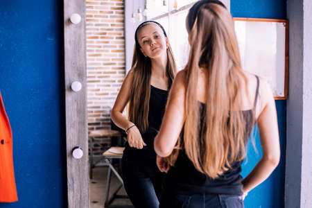 A young woman looks at her reflection in the mirror. The girl is in a good mood, smiling. Fashionable modern look.の写真素材