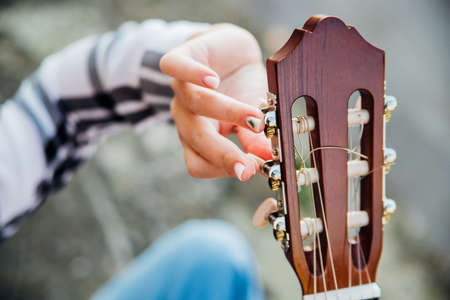 The girl tunes the guitar. Female hands close-up twist clips on the guitar. Learning music. Composer and author.の写真素材