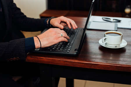 A young businessman is working at a computer in a cafe. Male hands close-up, typing on a laptop. Freelance. Work on remote access.の写真素材