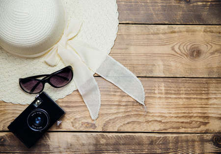 Summer straw hat, sunglasses, camera on a wooden background. Summer time, vacation, travel, tourism. Top view, space for text.の写真素材