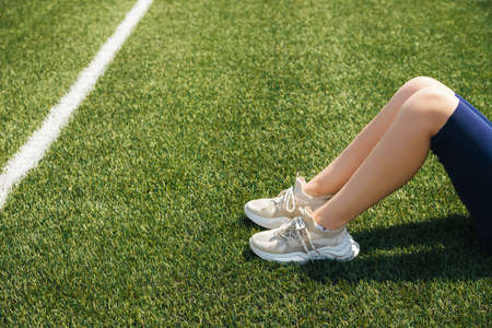 The legs of a girl in white sneakers on green artificial grass. Sports shoes. An active lifestyle....