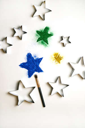 Abstract texture of small sequins in the shape of a star. Brilliant festive background. Multicolored sequins on a white background. Metal mold and brush.の写真素材