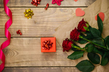 Top view, red gift box. Festive atmosphere, bouquet of red roses, satin ribbon and bows on a wooden background.の写真素材