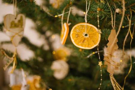 Wooden toys and a slice of dried orange hang on a green branch of a fir tree. Holiday decorations. Handmade toys. Christmas and New Year.の写真素材