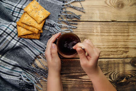 Women's hands hold a cup of black coffee on a wooden background. Delicious cookies, a warm scarf, a...