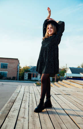 A young beautiful girl in a dress and a hat is spinning and dancing on a wooden podium. freedom of movement. joyful emotions.の写真素材