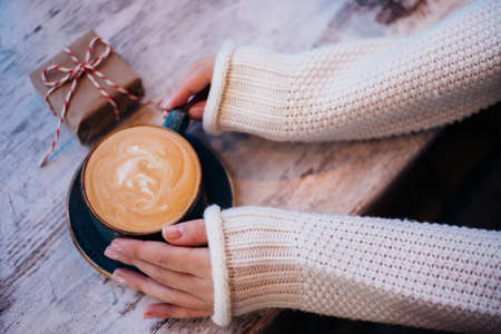 Women's hands are holding a cup of coffee. The atmosphere of a cozy evening. Hot drink. A girl in a...