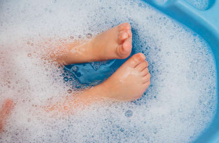 Baby feet in a blue bubble bath. Baby detergent, hygiene. baby skincare. Background and texture of soap bubbles.の写真素材