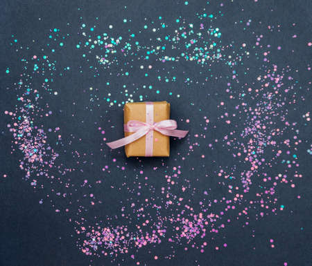 A small gift box with a pink satin bow on a dark gray background. Sparks are scattered around. Festive background.の写真素材