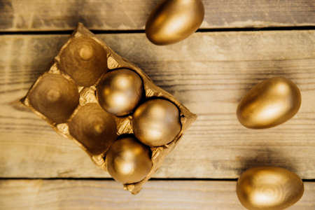 Top view Easter eggs painted with gold paint in a paper container on a wooden background. Festive...