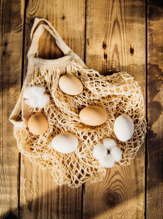 Easter concept. Beige mesh shopping bag with brown chicken eggs on a wooden background. Easter decorations. Sunlight and shadow.Eco-friendly bag material.の写真素材