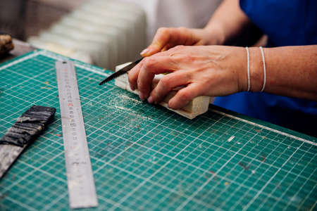 A female carpenter cuts wood with a knife in a carpentry or makeshift workshop. Dust and shavings...