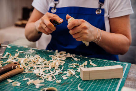 A female carpenter cuts wood with a knife in a carpentry or makeshift workshop. Dust and shavings scatter in the air.Workplace. Manufacture of wooden toys.の写真素材